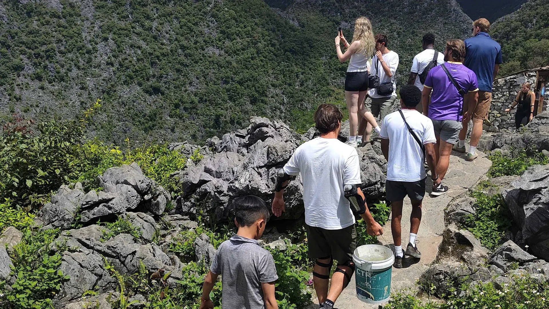 A small group walking a rocky limestone path to a viewpoint above a green karst valley