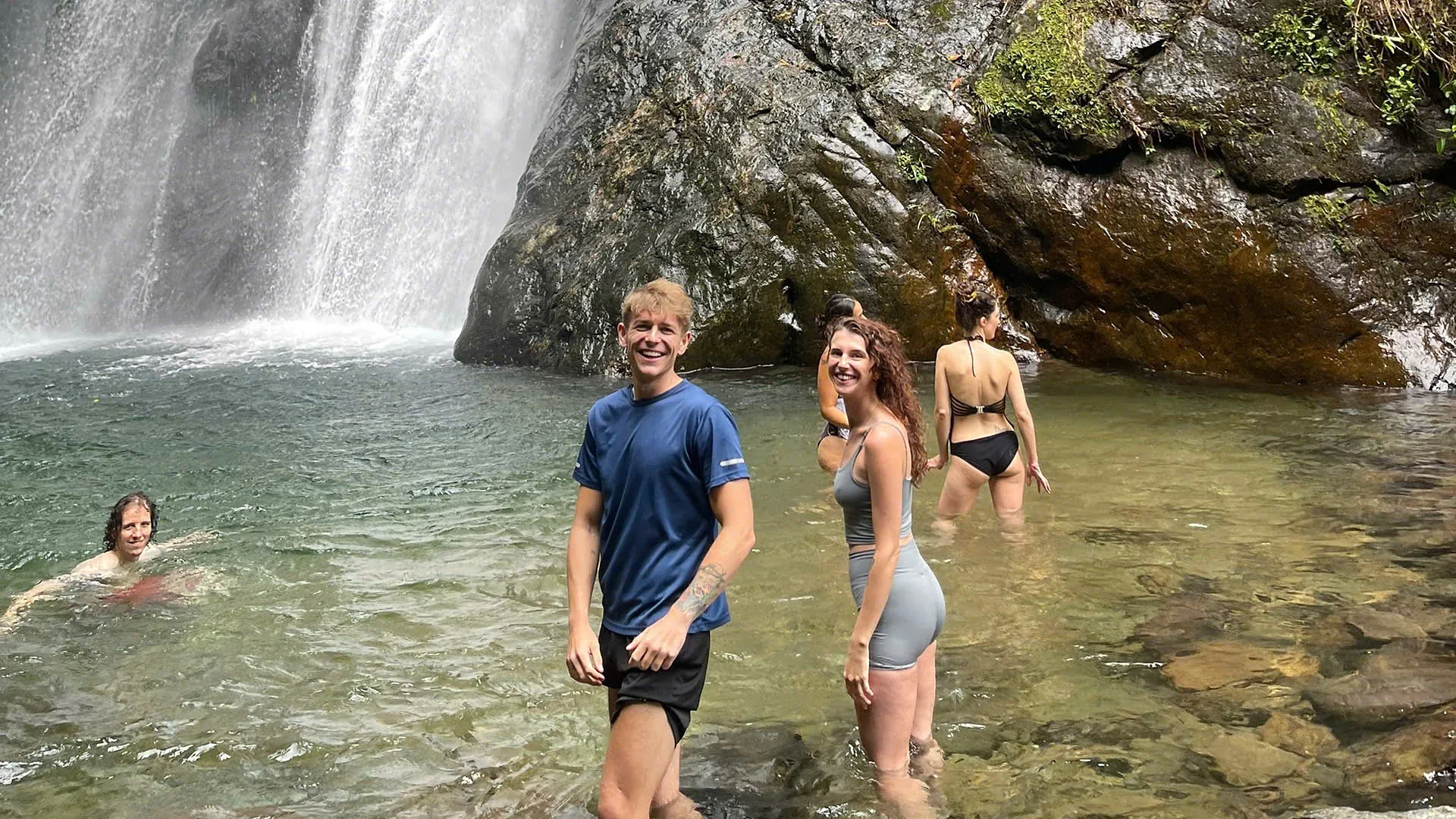 Guests wading and swimming in the cool pool below a waterfall on the first day of the Ha Giang Loop